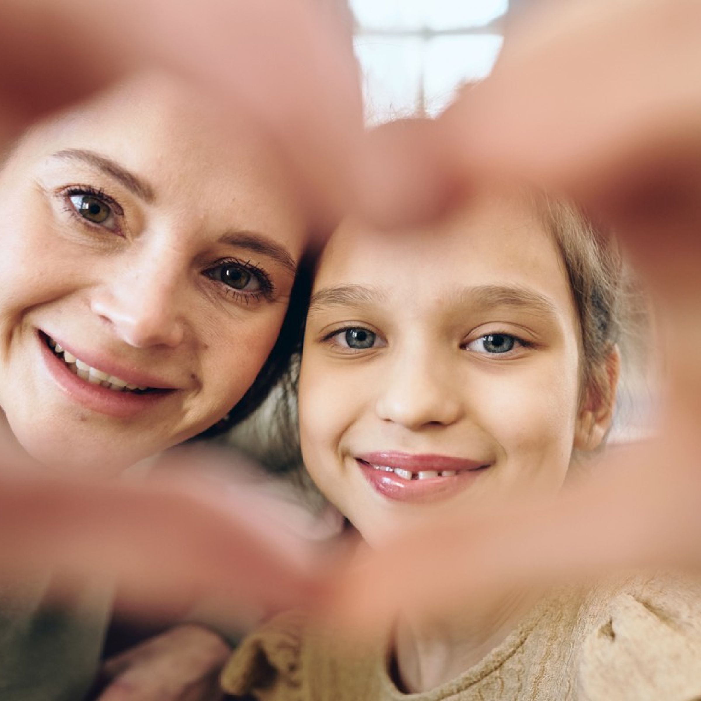 eine Frau und ein Mädchen bilden mit ihren Händen gemeinsam ein Herz, duch das sie schauen