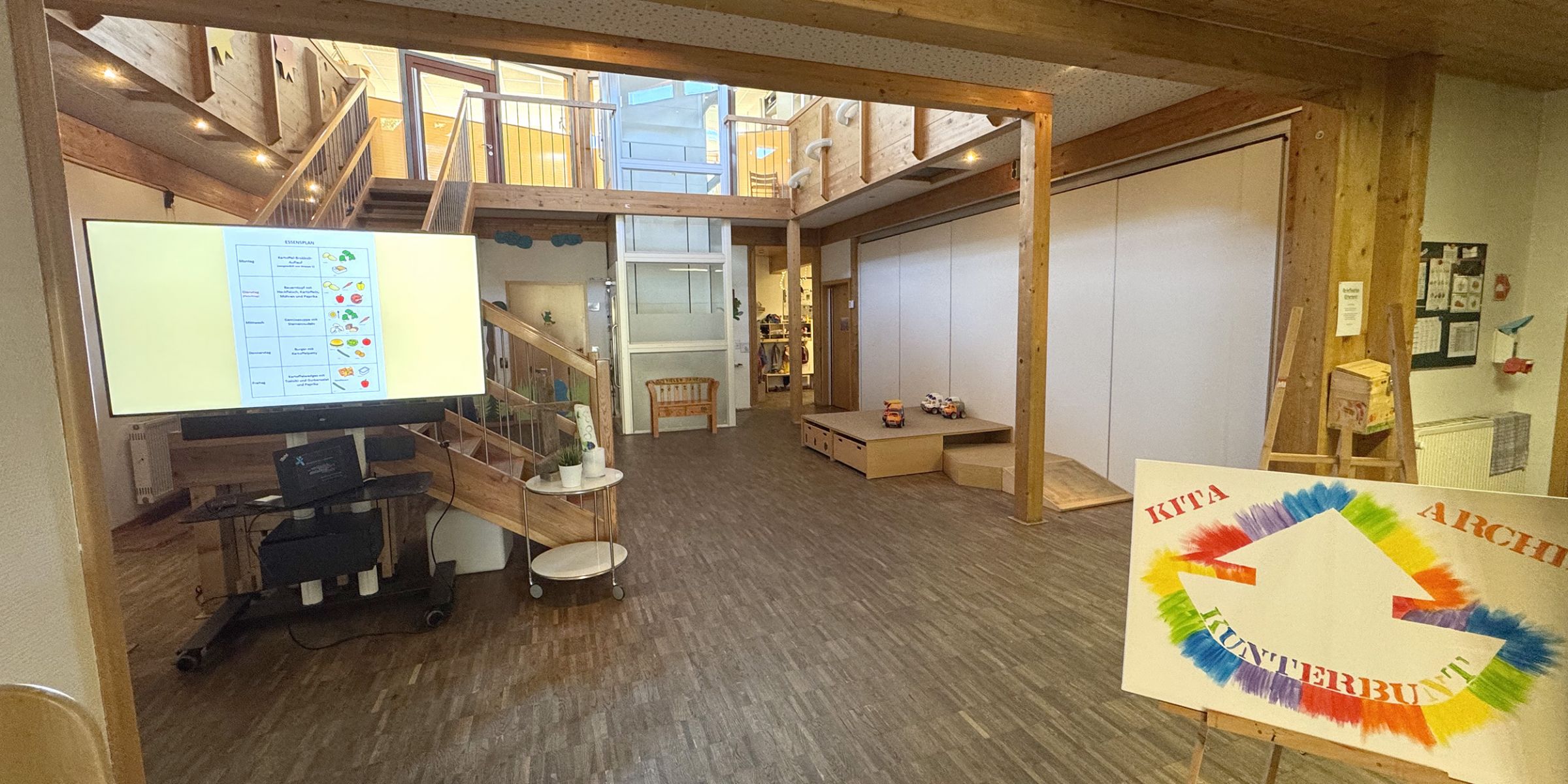 Der freundliche und helle Eingangsbereich der Kita Arche Kunterbunt in Monheim mit Parkett und Holzdecke