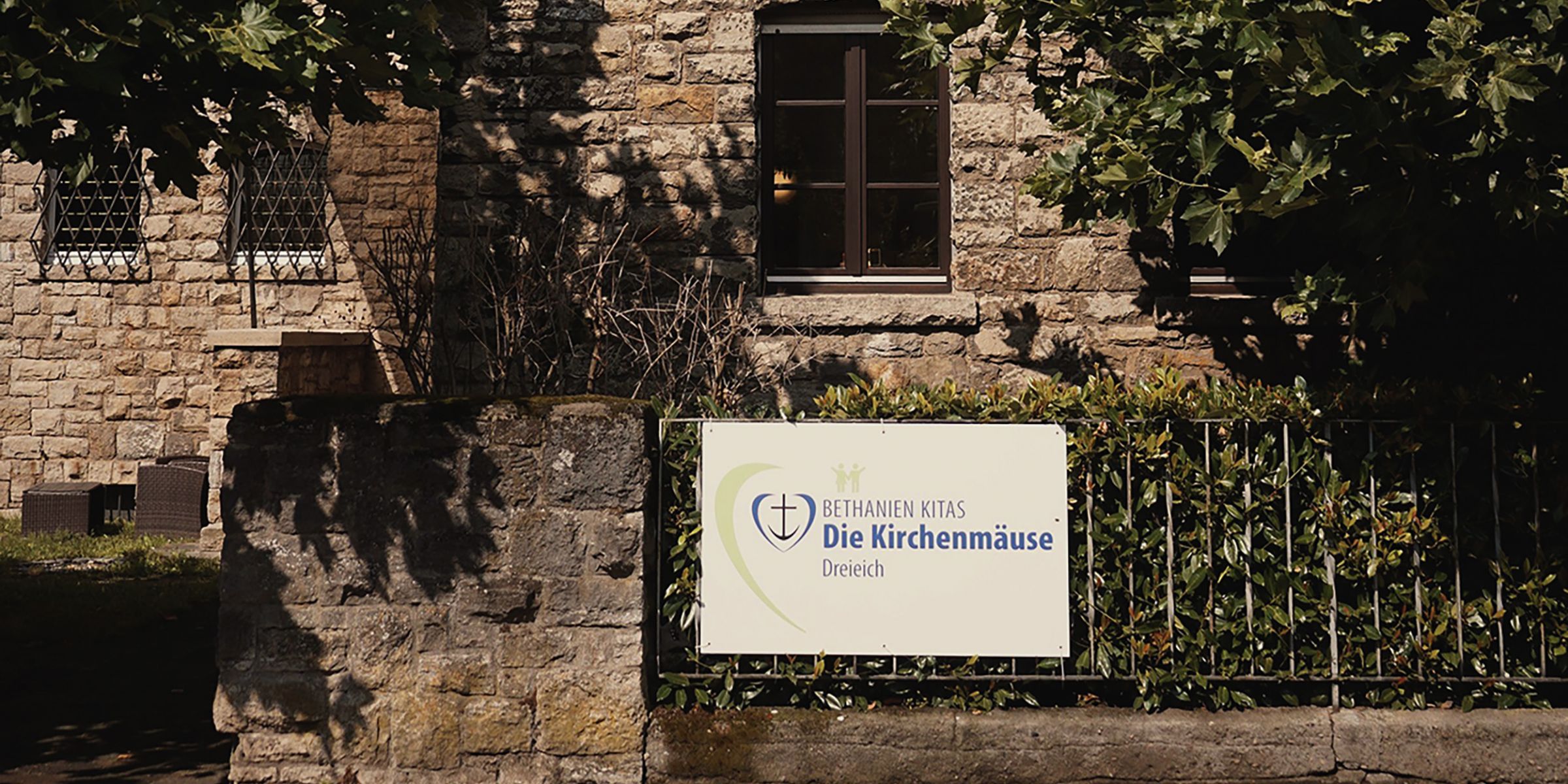 Die Hausfront des Kita Gebäudes mit dem Schild des Logos der Kita Die Kirchenmäuse. 