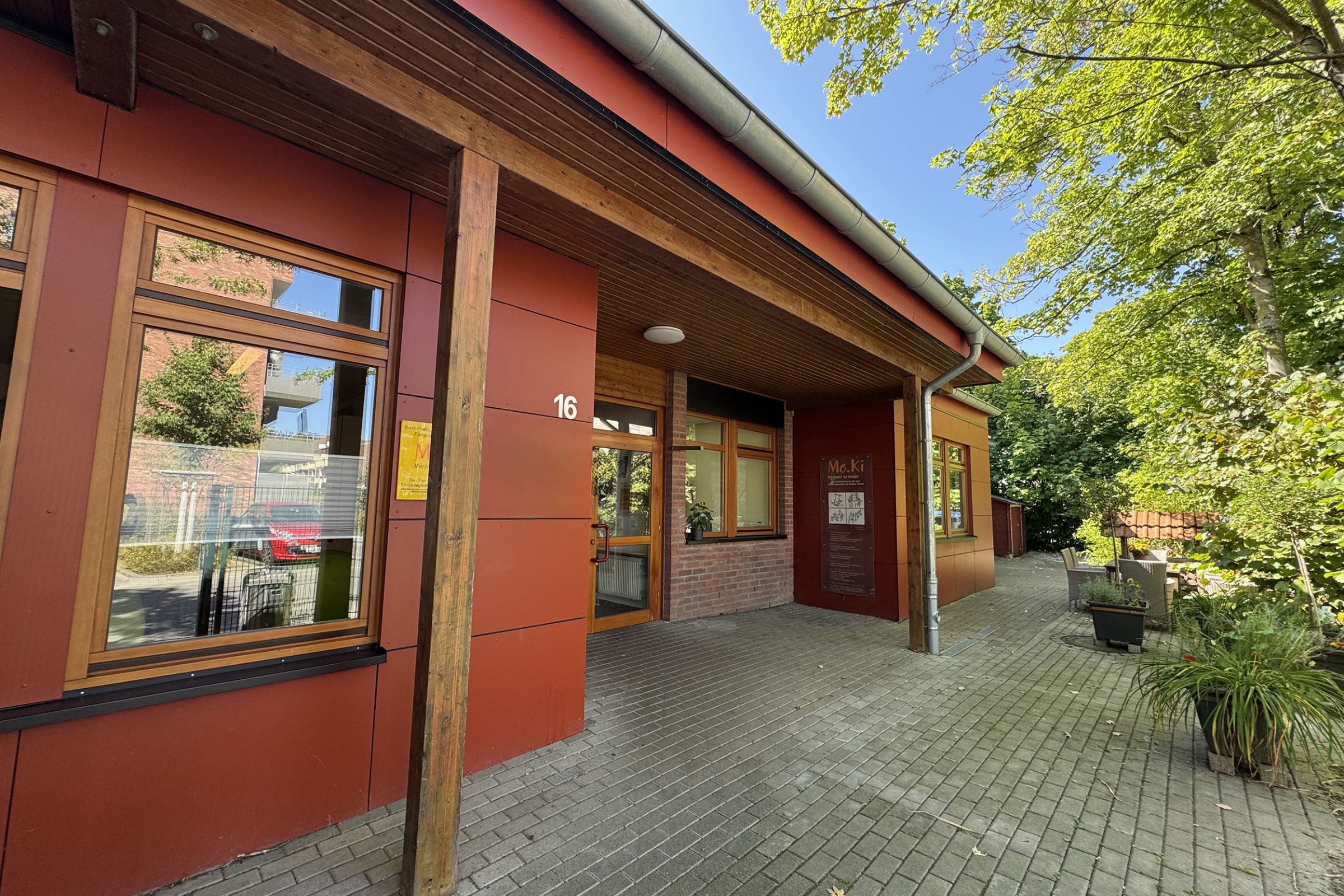 Der Eingangsbereich außen der Kita Arche Kunterbunt in Monheim mit roten Wänden, Holzbalken und Backstein