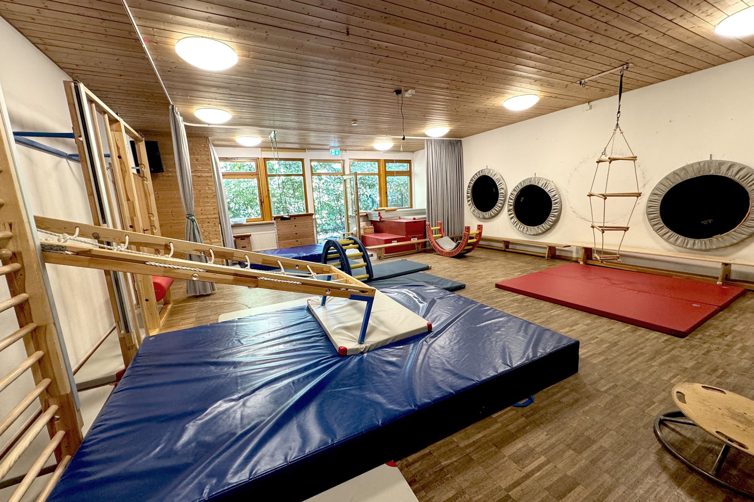 Der Turnraum der Kita Arche Kunterbunt in Monheim, mit Holzboden, dicken blauen Turnmatten, Klettergerüsten aus Holz und viel Platz zum Turnen und Toben.