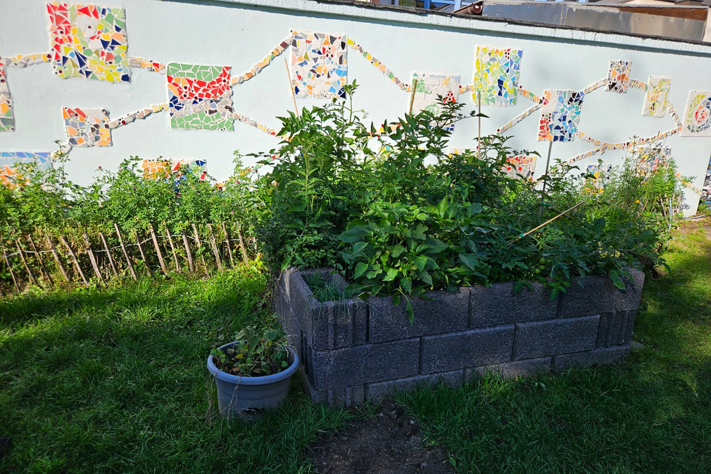 Der kleine Garten der Kita Scharrenberger Straße mit Hochbeet vor einer bunt gestalteten Mauer.