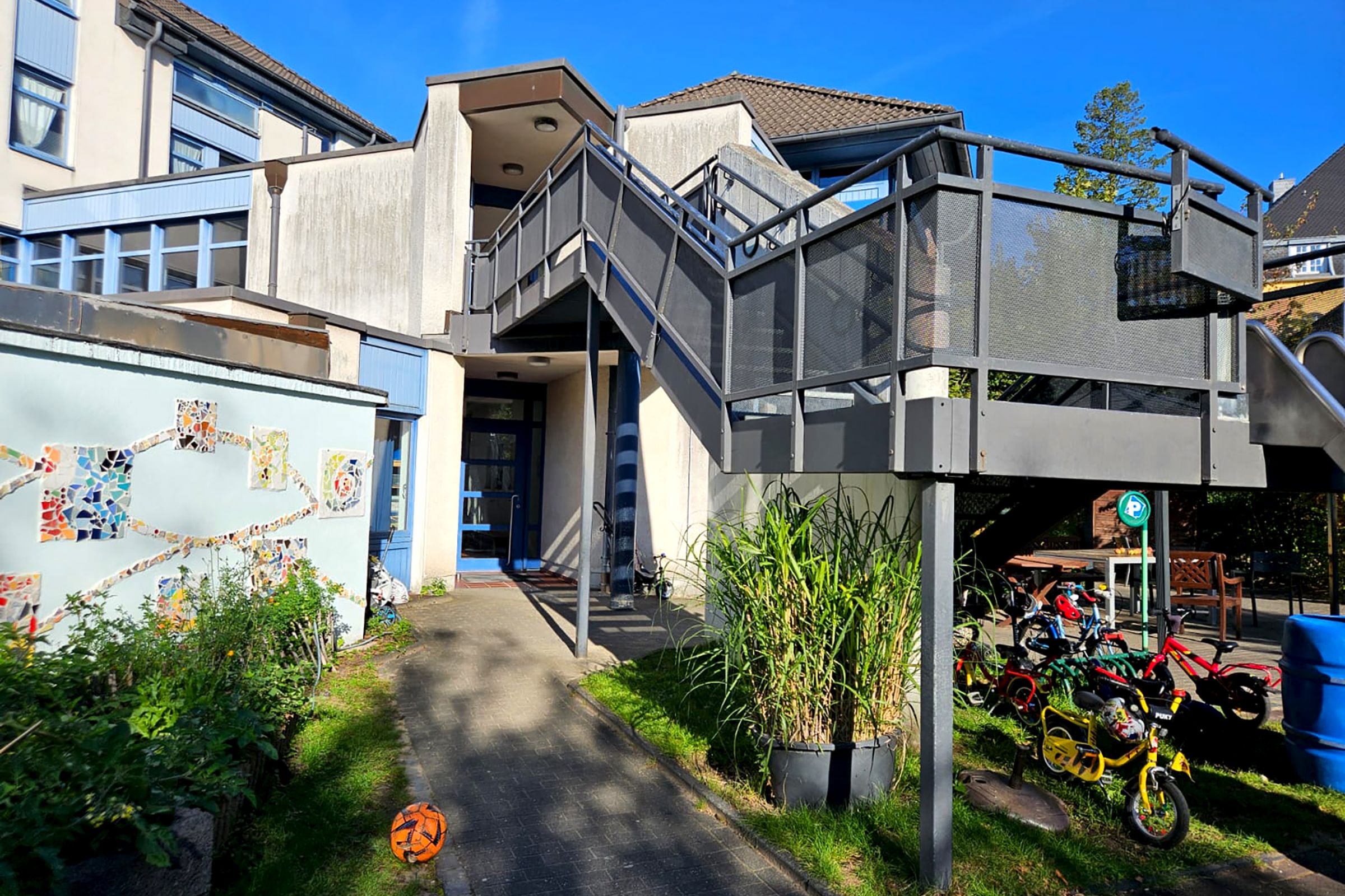 Außenansicht und Eingangsbereich der Kita Scharrenberger Straße in Solingen, mit kleinem Vorgarten und Außentreppe.