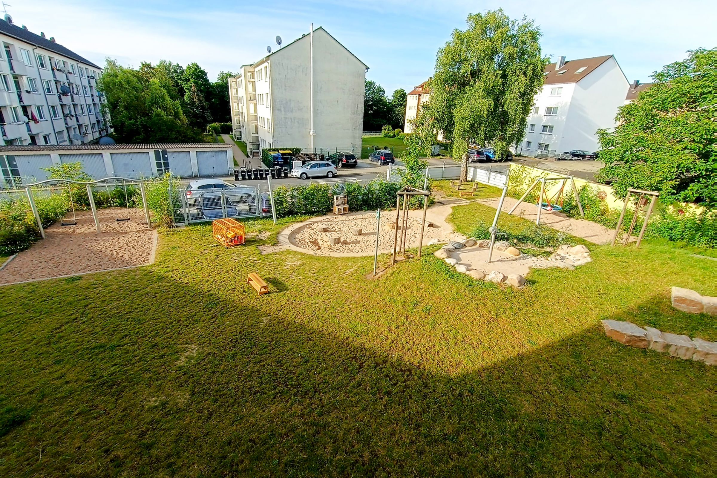Das Außengelände der Kita, mit Sandkasten, Nestschaukel, Schaukeln und Spielgeräten