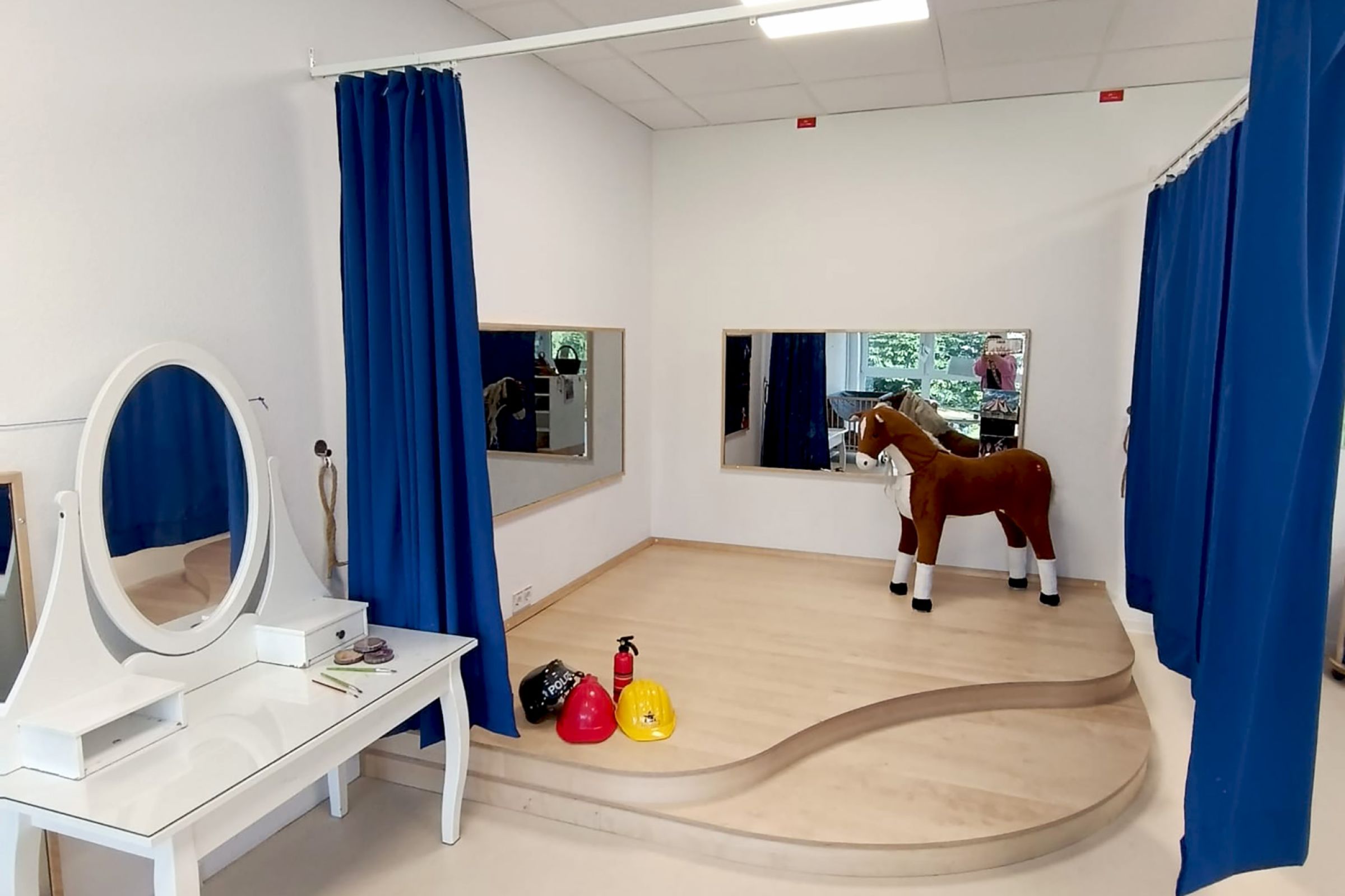 Ein Verkleidungsecke mit Spiegeln, Vorhängen, Kostümen und einem Schminktisch. 