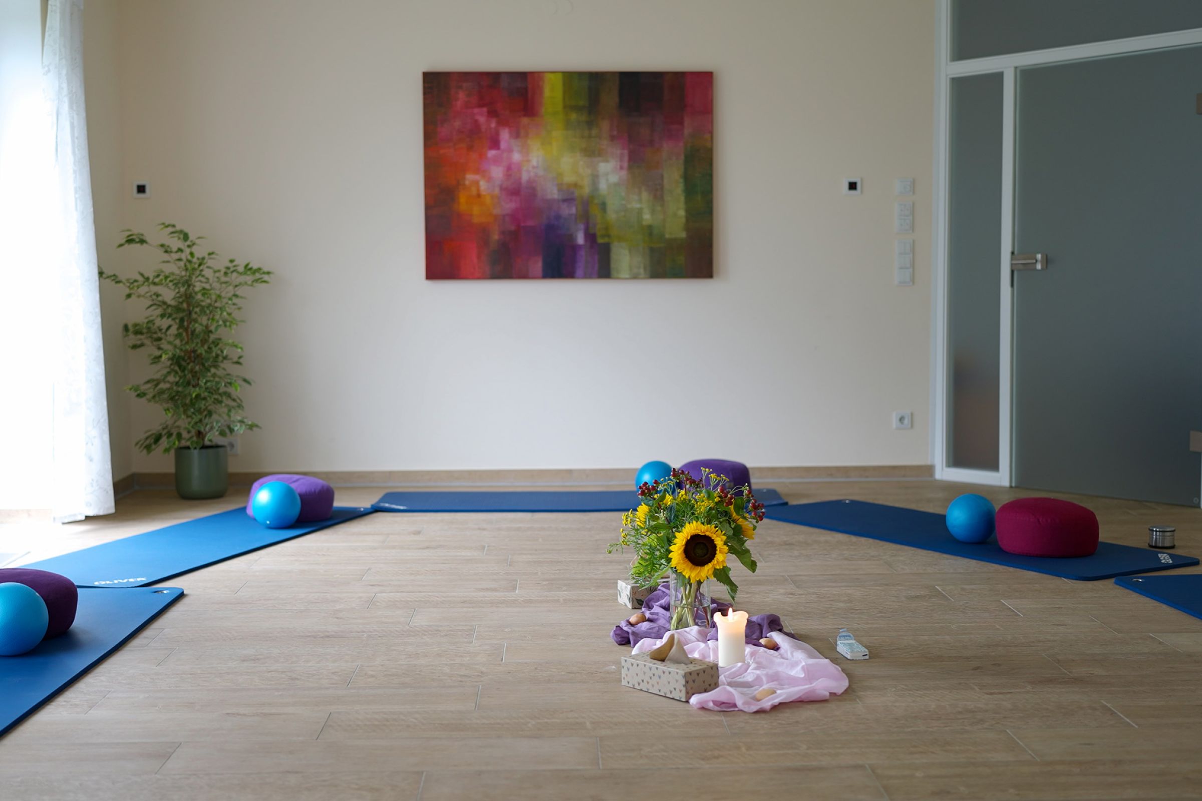 Ein Raum der Beratungsstelle mit einem gemütlichen Sofa, einem Bücherregal und Stühlen. In der Mitte des Raumes steht ein kleiner Tisch mit Blumen, Taschentüchern und einer kleinen Kerze. 