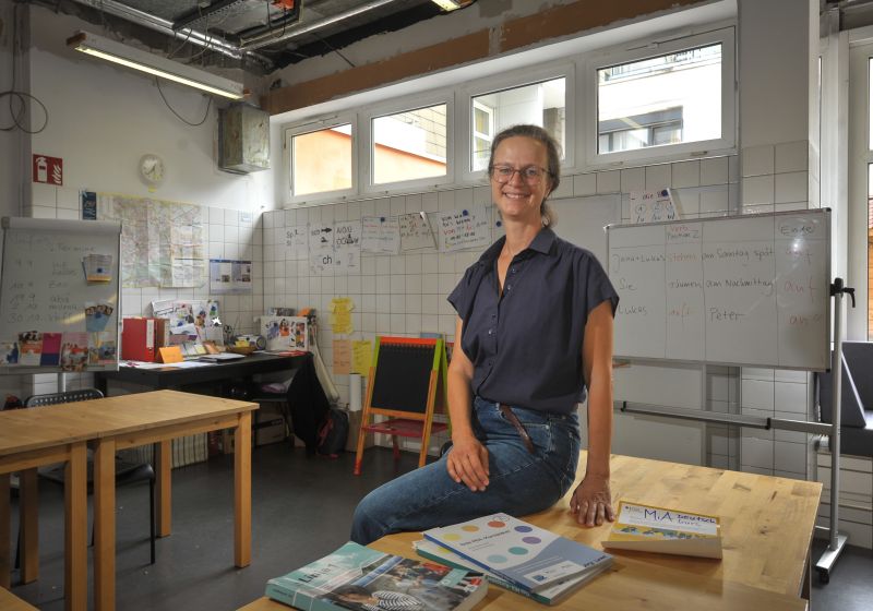 Antje Wooge sitzt auf einem Holztisch im Jugendzentrum und lächelt