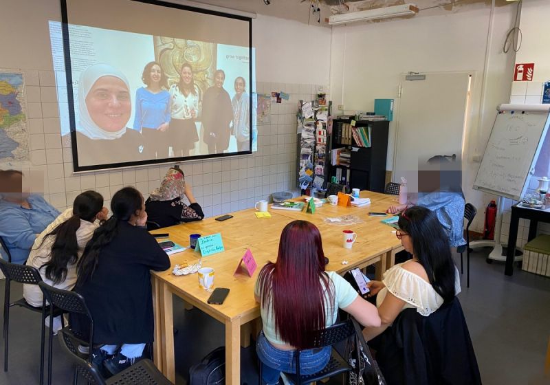 Eine Gruppe von fünf Frauen sitzen rund um einen Holztisch im Jugendzentrum basement26