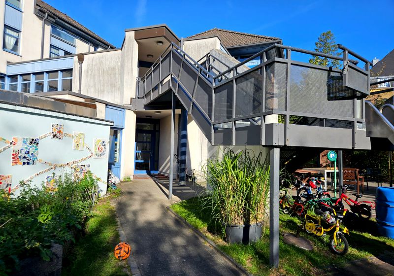 Außenansicht und Eingangsbereich der Kita Scharrenberger Straße in Solingen, mit kleinem Vorgarten und Außentreppe.