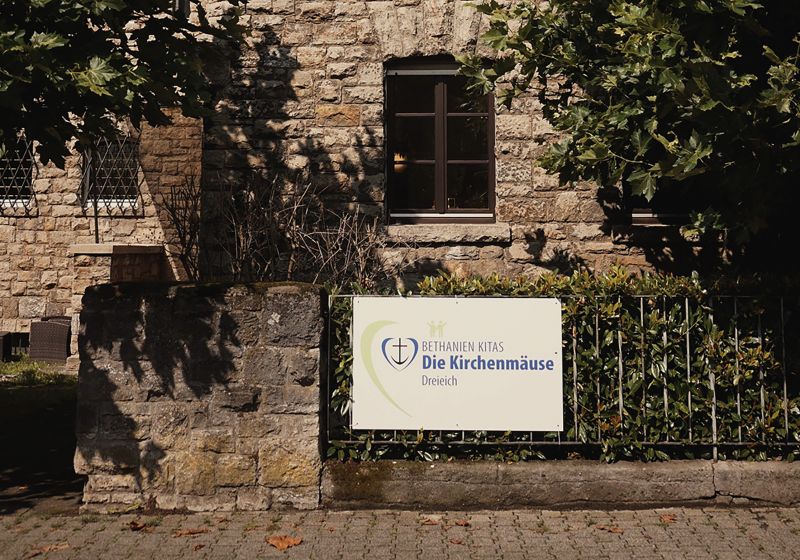 Die Hausfront des Kita Gebäudes mit dem Schild des Logos der Kita Die Kirchenmäuse. 